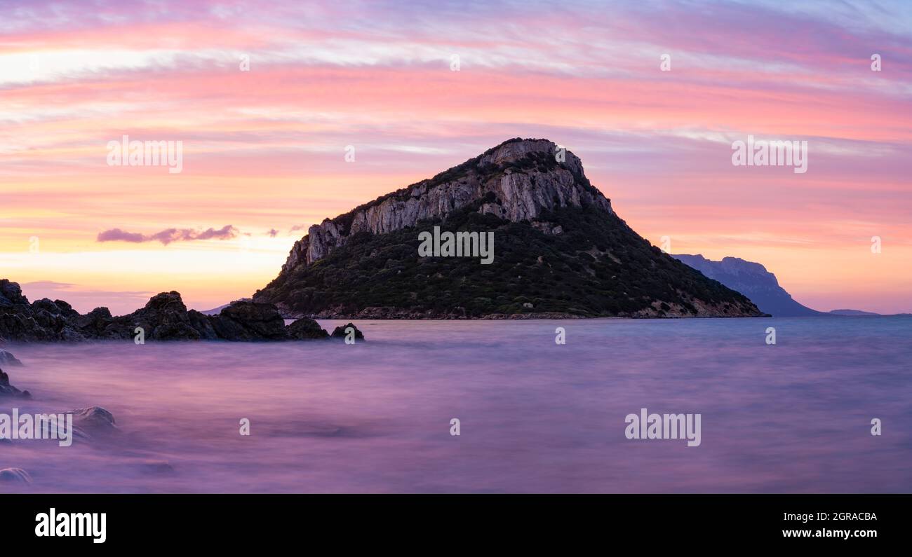 Atemberaubender Blick auf die Insel Figarolo bei einem romantischen und entspannenden Sonnenaufgang, der sich auf einem ruhigen Wasser im Vordergrund widerspiegelt. Golfo Aranci, Sardinien. Stockfoto