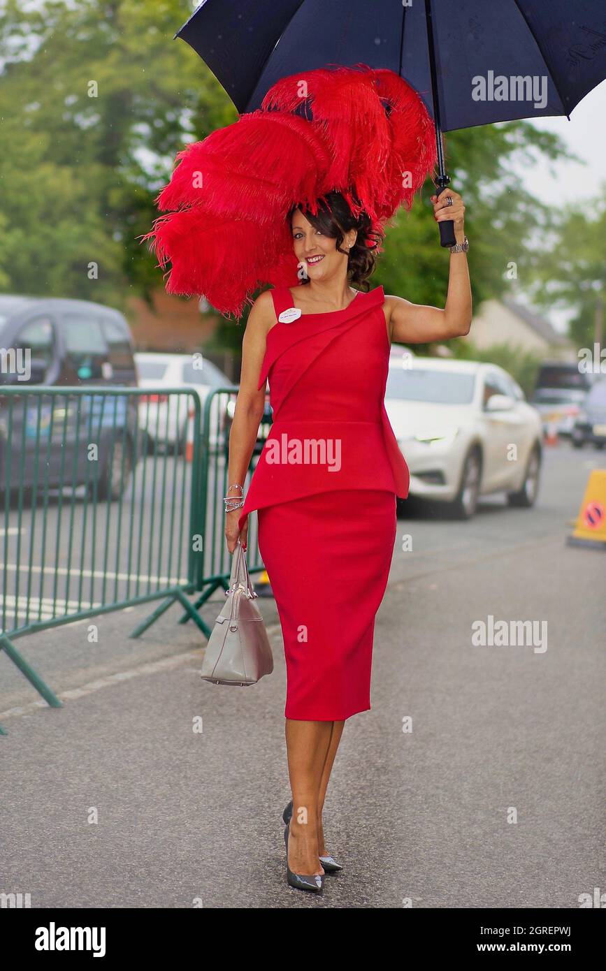 Elegante Dame mit Regenschirm in einer stilvollen roten Kombination kommt auf der Rennbahn Ascot an Stockfoto