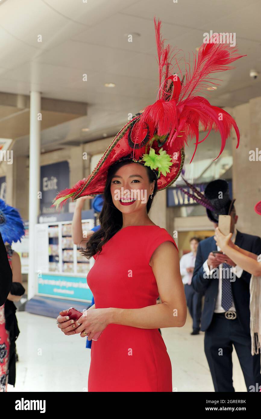 Die elegante Dame an der Waterloo Station trägt ein rotes Kleid und einen schicken Hut, bevor sie zur Ascot Racecourse geht Stockfoto