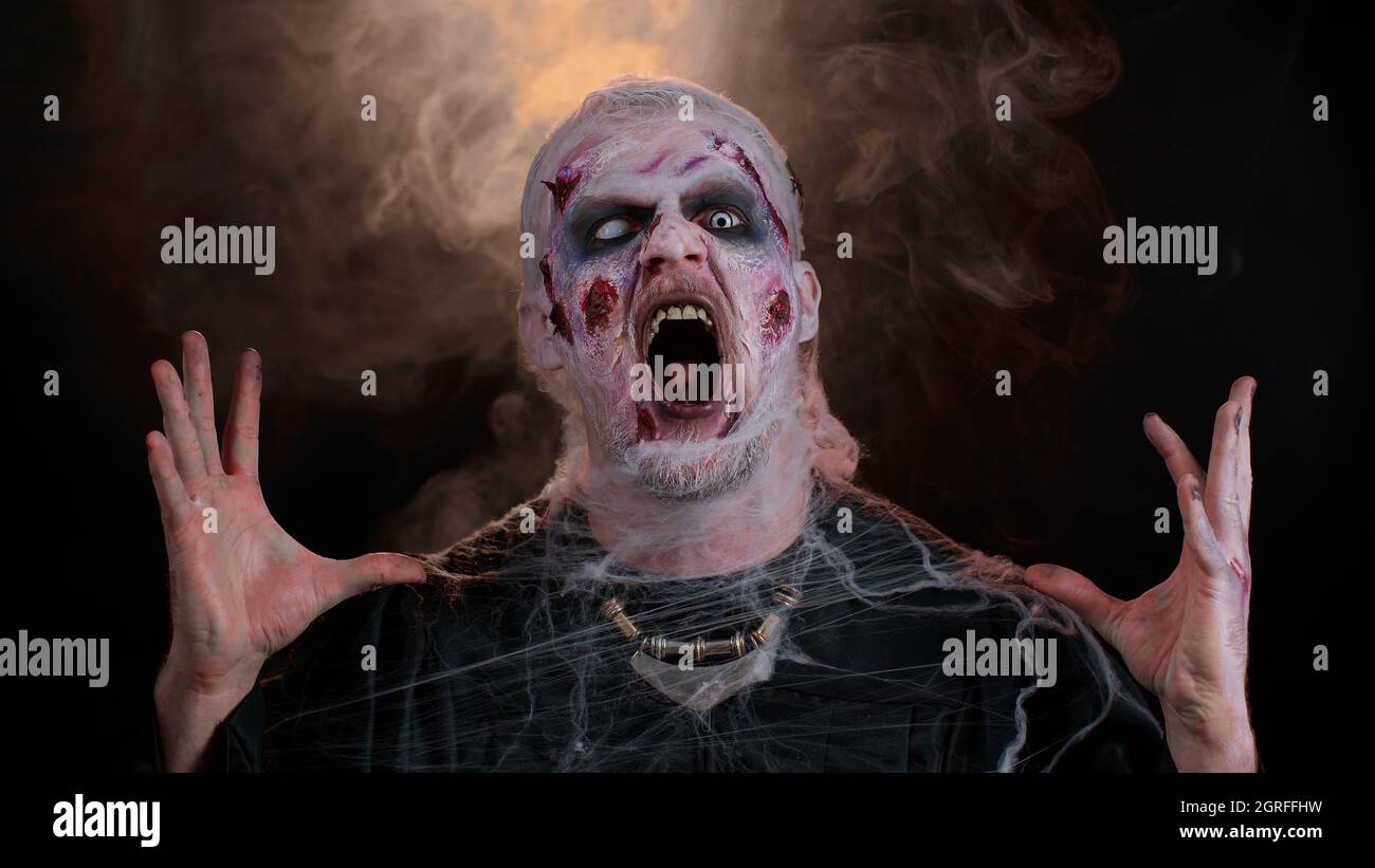 Zombie-Mann mit Wunden Narben und Kontaktlinsen Blick auf Kamera klickt seine Zähne versuchen, zu verzagen Stockfoto