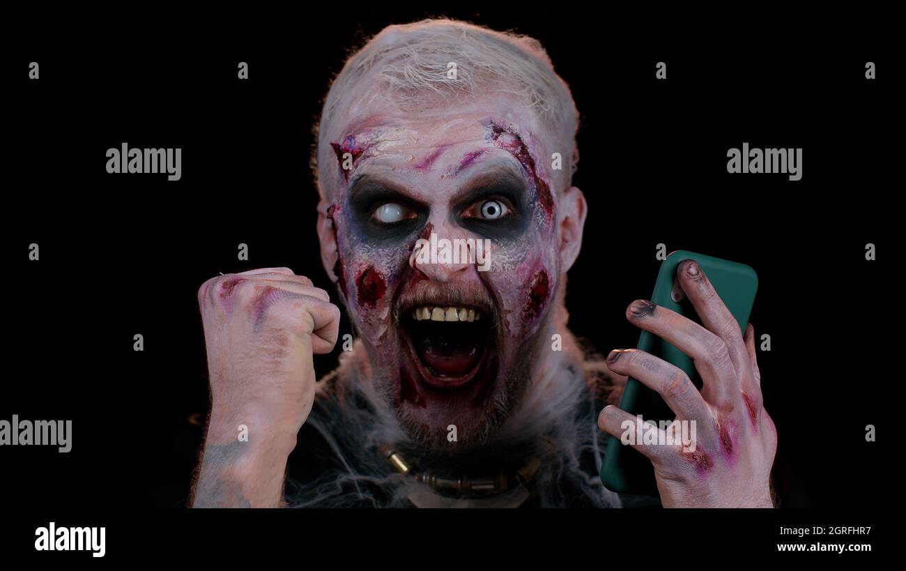 Glücklich aufgeregt finsteren Mann Halloween Zombie verwenden Smartphone feiert Lotteriegewinn, Erfolg Glück Stockfoto