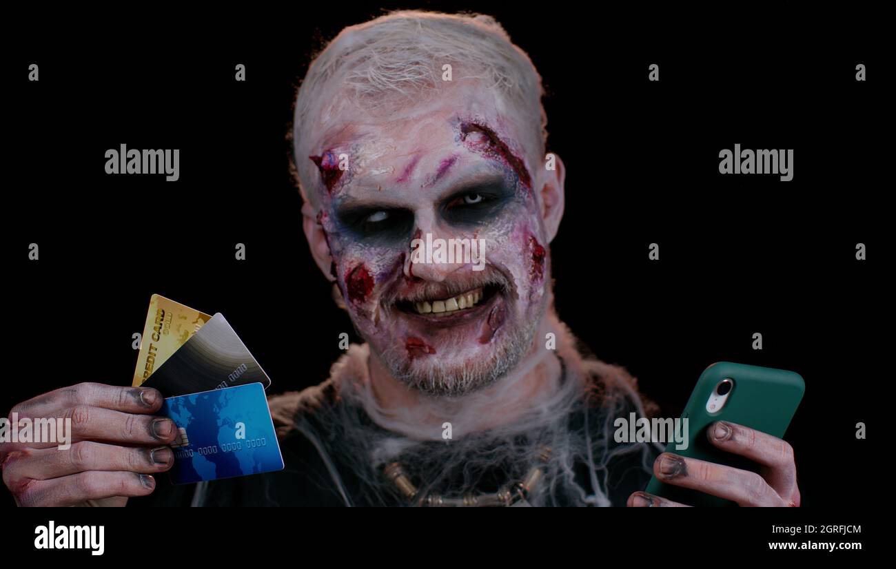 Finsterer Mann Halloween Zombie mit Kreditkarten und Smartphone, während Einkäufe online einkaufen Stockfoto