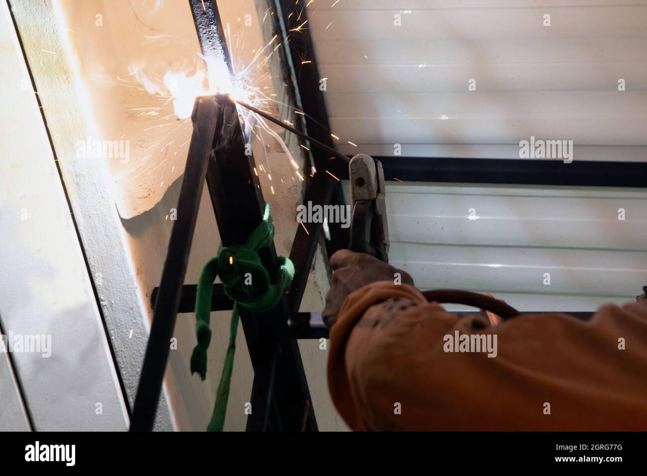 Ein asiatischer Arbeiter schweißen eine Stahlmarkise an die Decke eines Hauses. Stockfoto