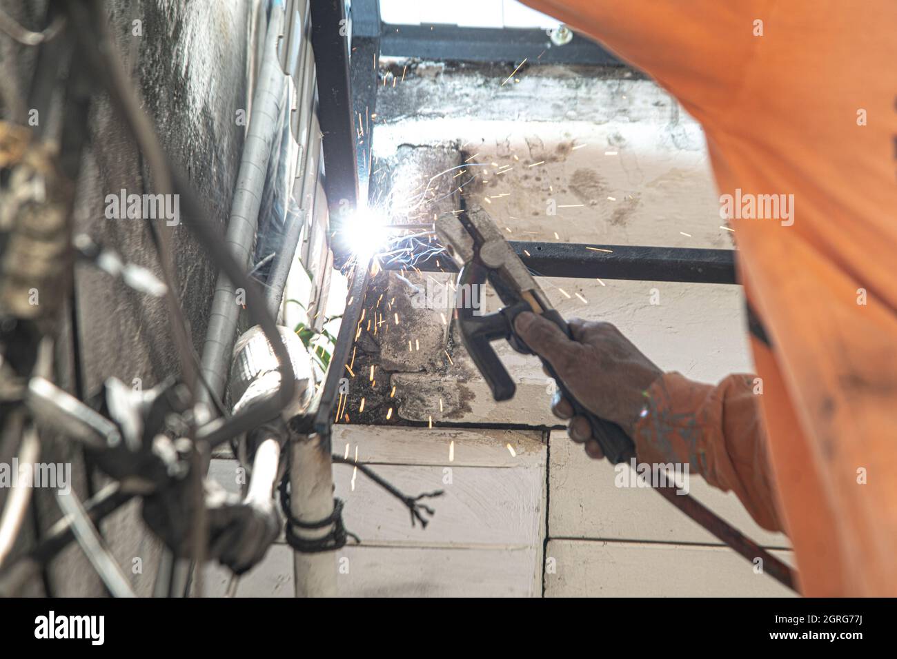 Ein asiatischer Arbeiter schweißen eine Stahlmarkise an die Decke eines Hauses. Stockfoto