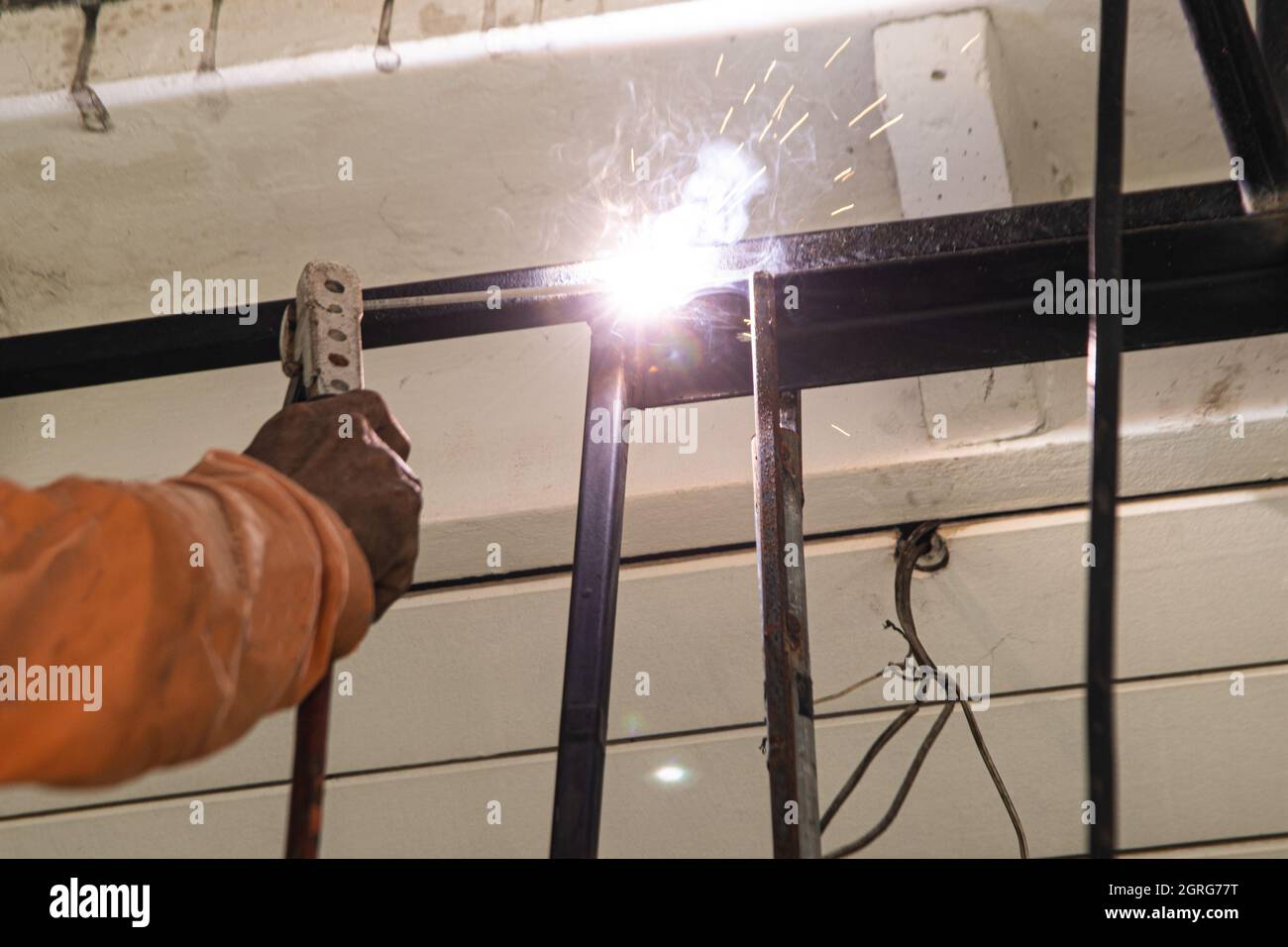 Ein asiatischer Arbeiter schweißen eine Stahlmarkise an die Decke eines Hauses. Stockfoto