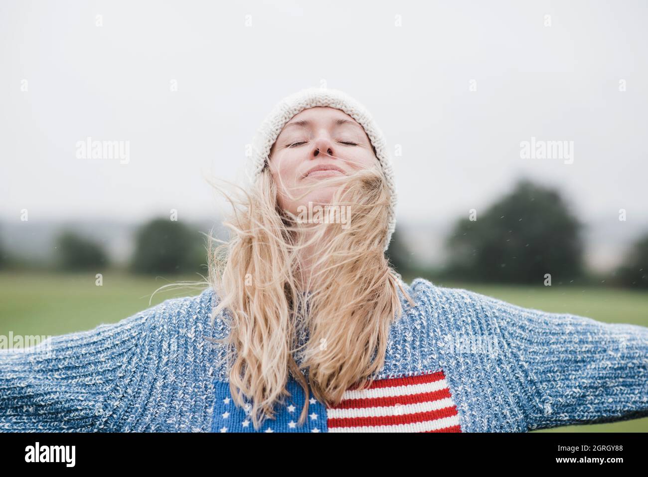 Die Frau trägt die amerikanische Flagge und genießt den Wind und den Regen in ihren Haaren Stockfoto
