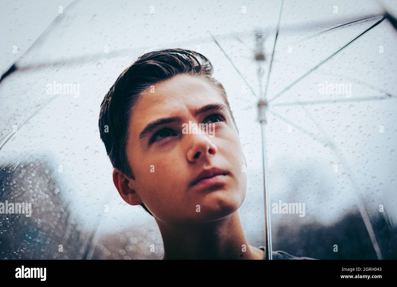 Nahaufnahme eines Teenagerjungen unter einem Regenschirm. Stockfoto