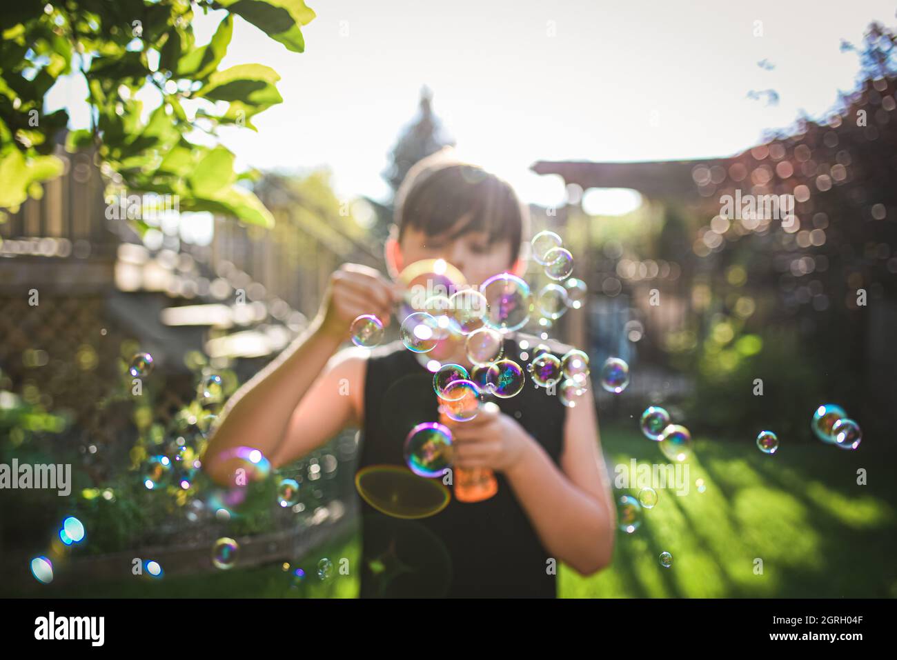 Kleiner Junge, der an einem sonnigen Tag Blasen in einem Hinterhof bläst. Stockfoto