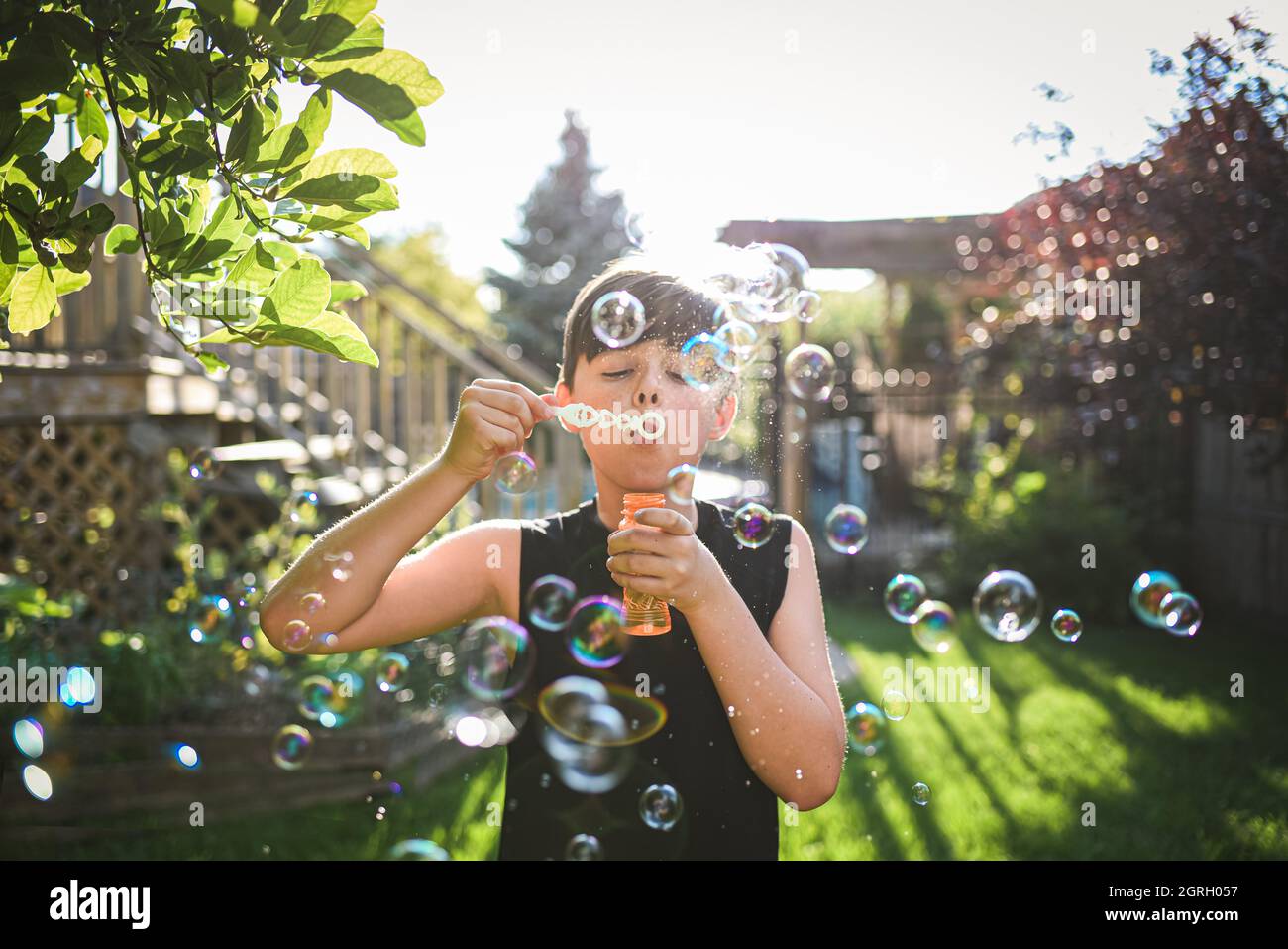 Kleiner Junge, der an einem sonnigen Tag Blasen in einem Hinterhof bläst. Stockfoto