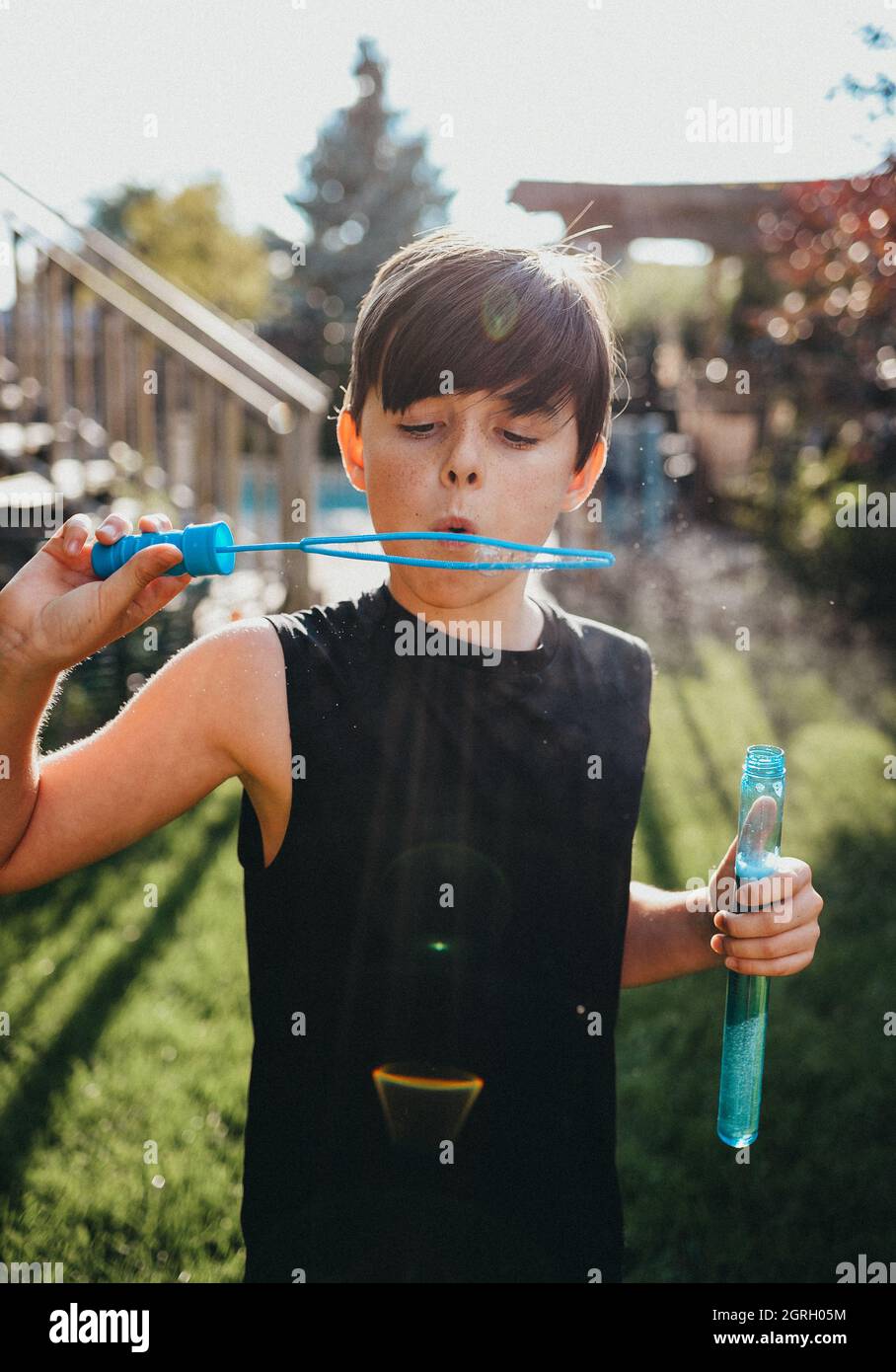 Kleiner Junge, der an einem sonnigen Tag Blasen in einem Hinterhof bläst. Stockfoto