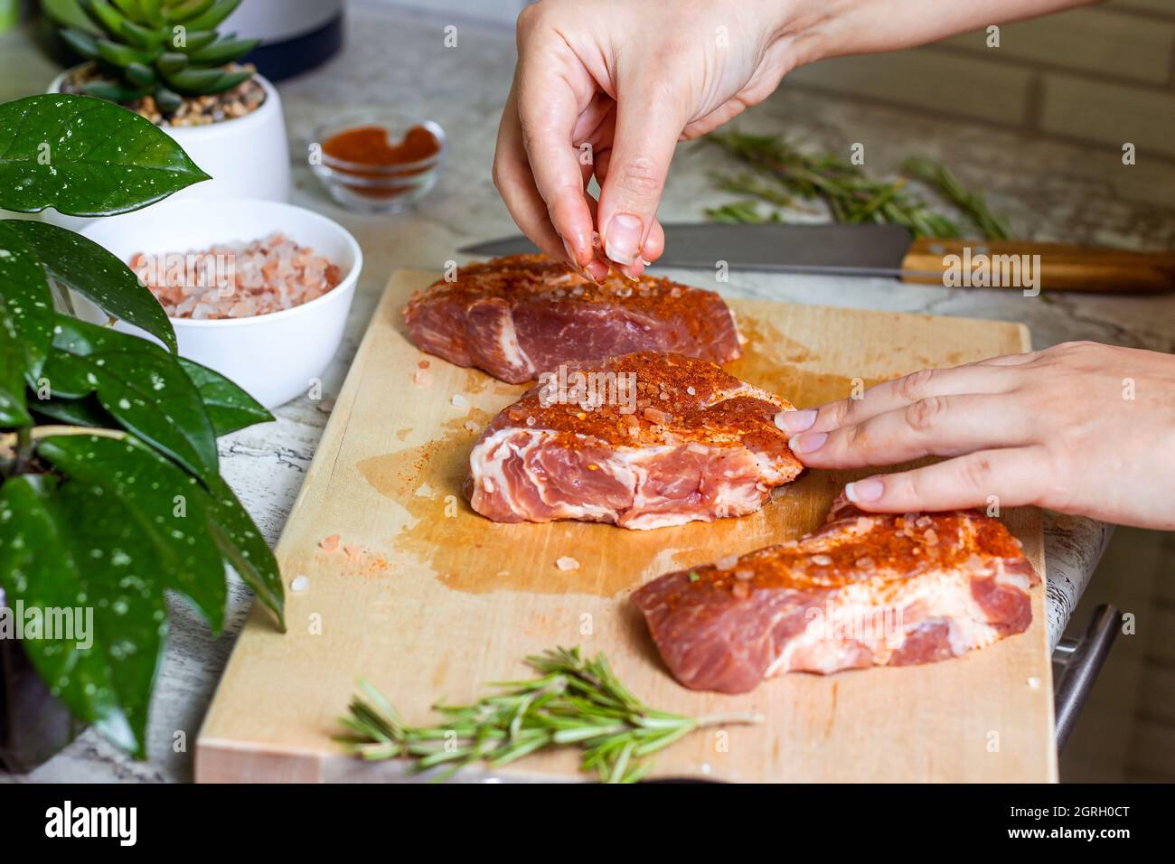 Rohes marmoriertes Rindersteak mit Salz und Gewürzen auf Holz-Schneidebrett-Hintergrund. Die Zubereitung eines frischen Fleisches zum Abendessen. Stockfoto