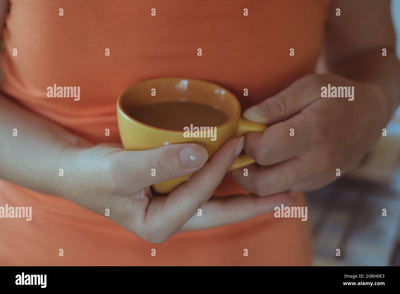 Frau in Orange hält eine Tasse Milchkaffee in den Händen Stockfoto