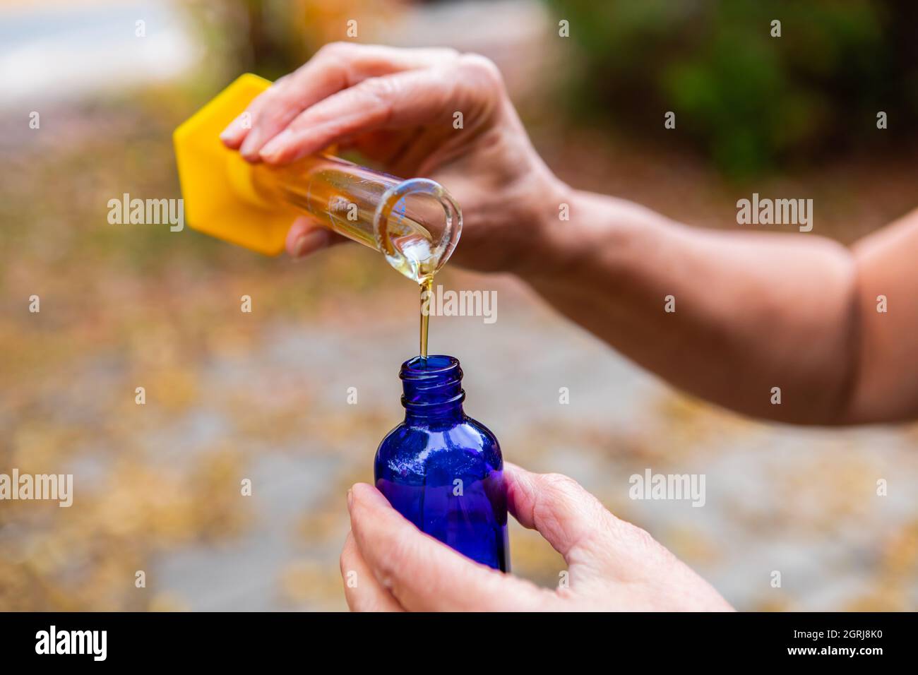 Hände einer Person , Gießen eines ätherischen Öls für die Aromatherapie, von einem transparenten Kolben zu einem blauen Fläschchen, für die Gesundheit und Entspannung verwendet. Stockfoto