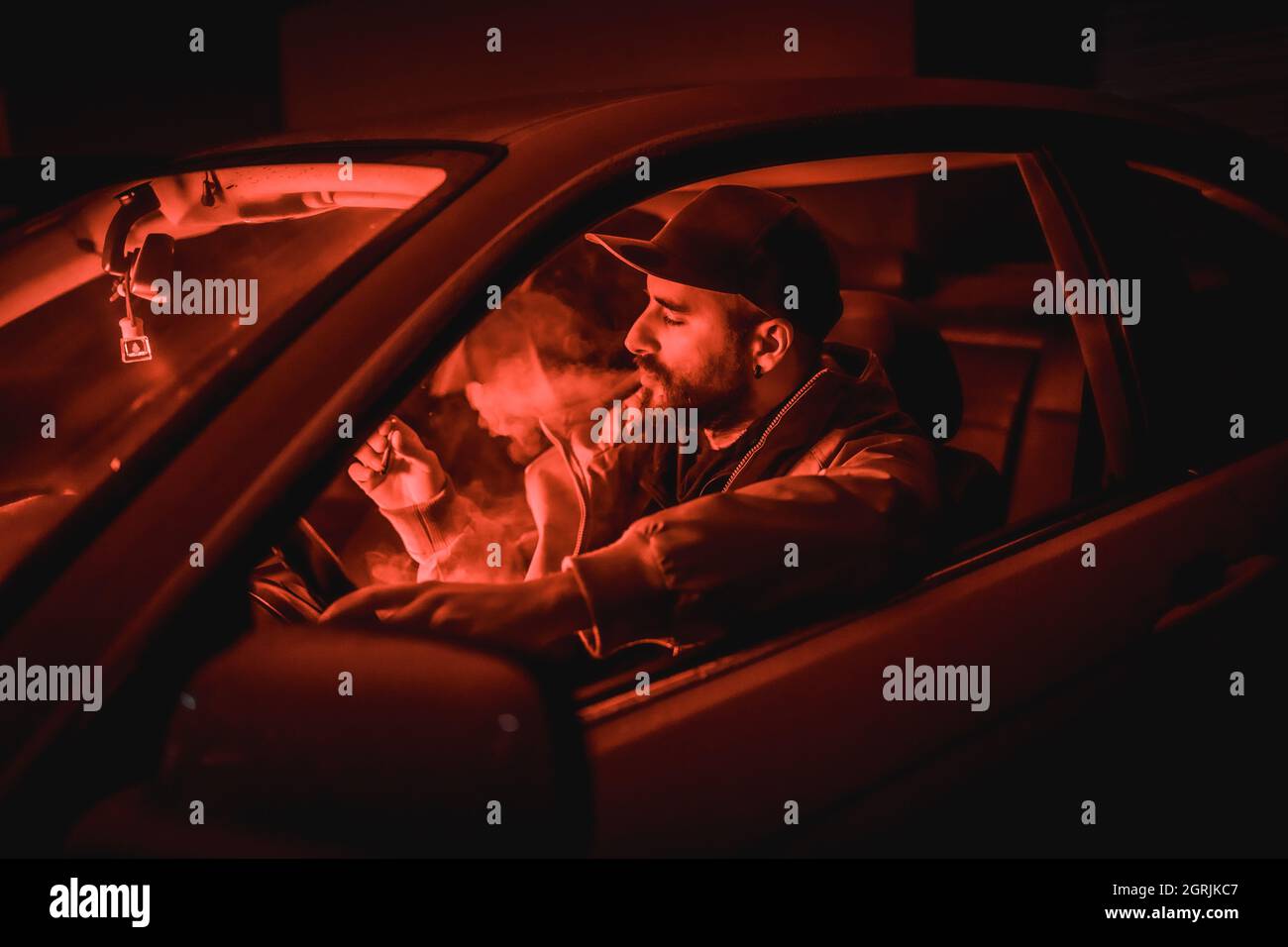 High-Angle-Aufnahme eines kaukasischen Mannes, der in einem Auto unter rotem Nachtlicht raucht Stockfoto