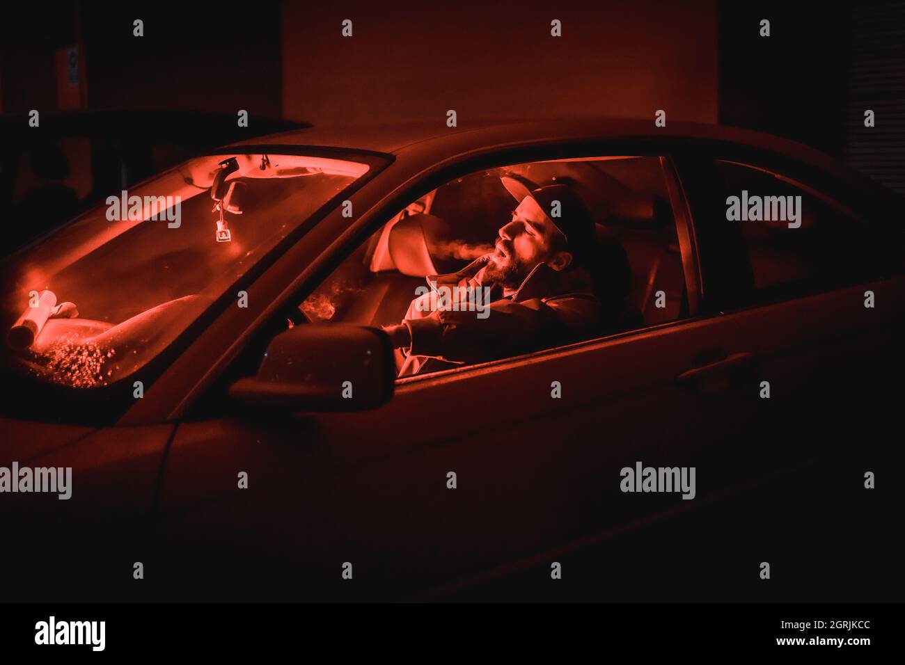 High-Angle-Aufnahme eines kaukasischen Mannes, der in einem Auto unter rotem Nachtlicht raucht Stockfoto