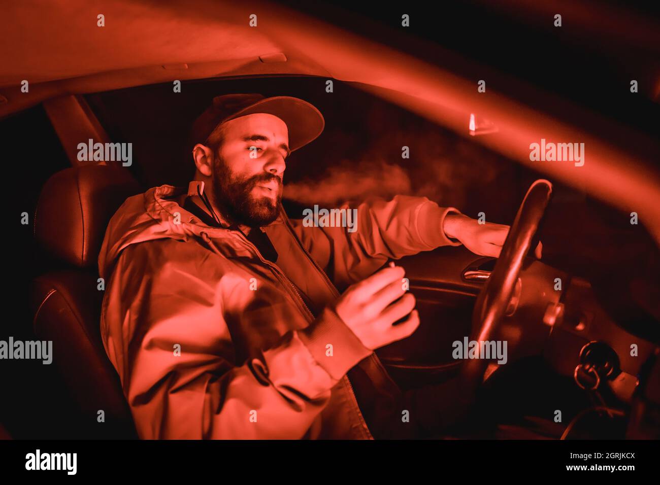 Nahaufnahme eines kaukasischen Mannes, der in einem Auto unter rotem Nachtlicht raucht Stockfoto