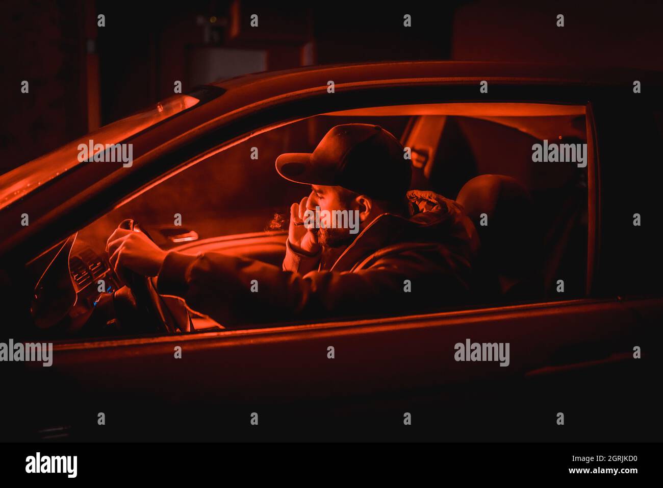 Nahaufnahme eines kaukasischen Mannes, der in einem Auto unter rotem Nachtlicht raucht Stockfoto