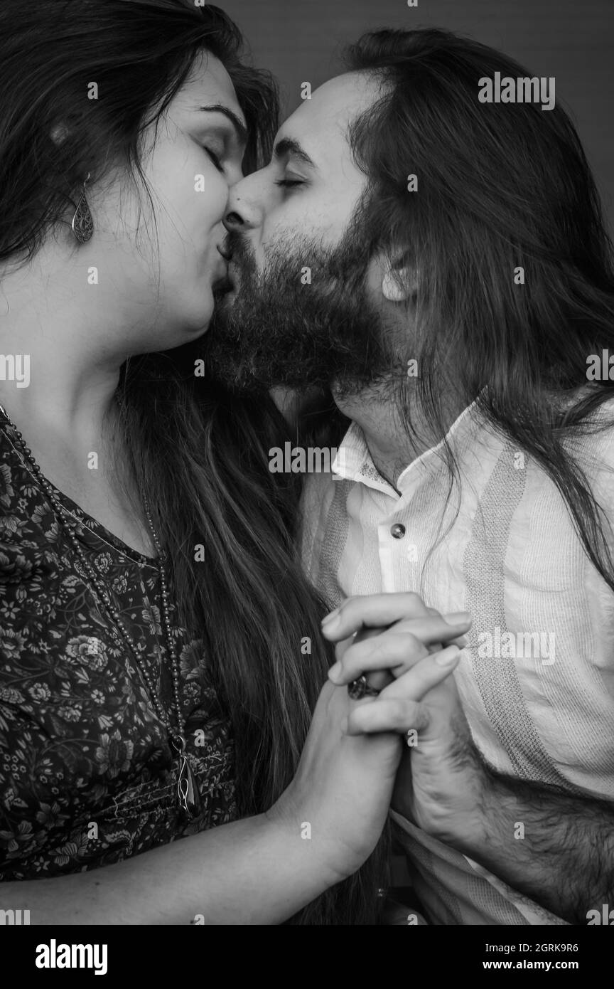 Schwarz-weißes Porträt eines jungen Paares, das sich in der Hand küsst, beide haben lange Haare und der Mann hat einen Bart Stockfoto