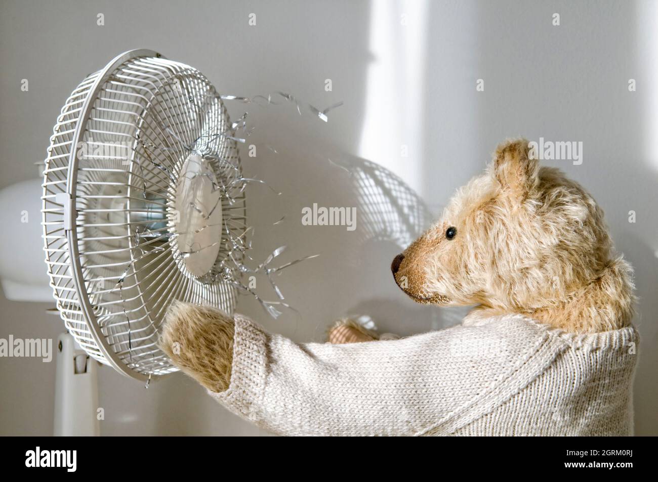Altmodischer Teddybär vor einem elektrischen Ventilator mit Lametta, der bläst Stockfoto