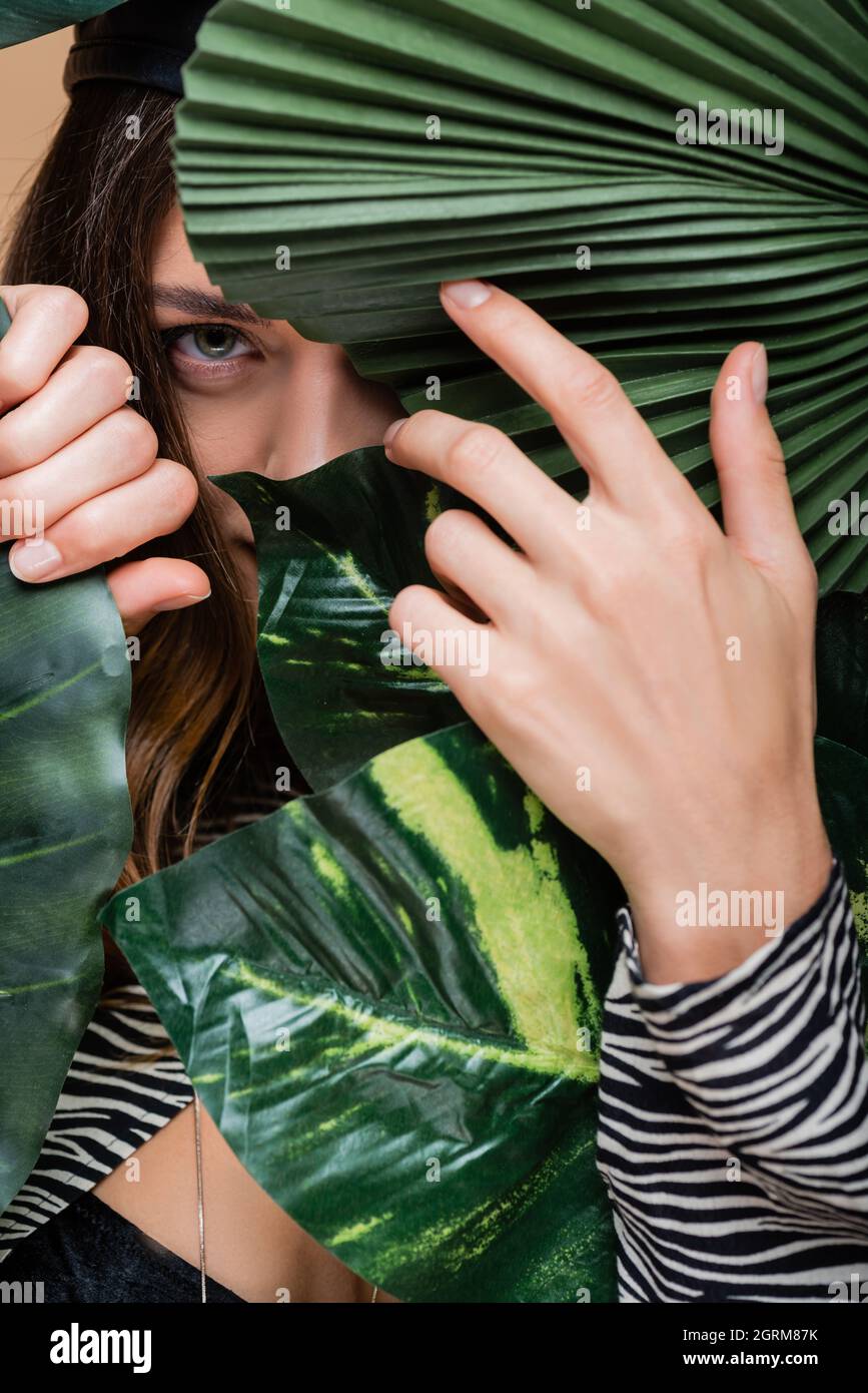 Junge Frau schaut durch grüne tropische Blätter auf die Kamera Stockfoto