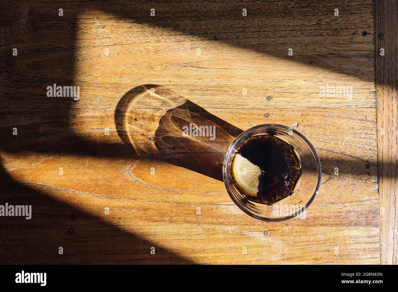 Trinkglas mit Cola-Getränk. Licht und Schatten auf Holztisch. Stockfoto