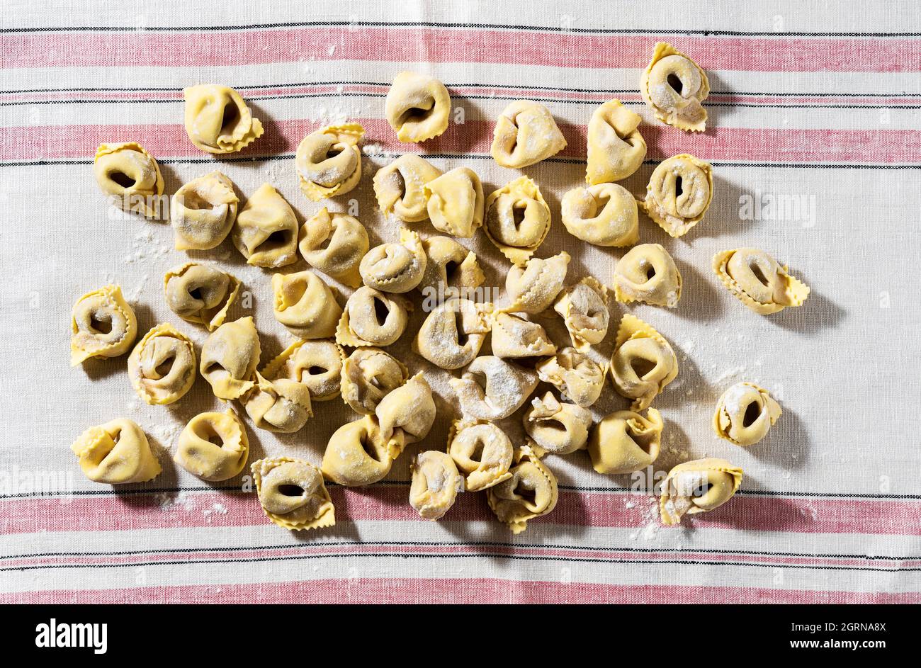 Rohe, frische, hausgemachte Ravioli auf einer rosa gestreiften Leinentischdecke Stockfoto