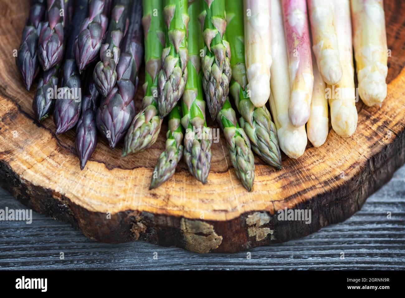 Grüner, violetter und weißer Spargel sprießt auf Holzbrett aus der Nähe. Draufsicht flach liegend. Food-Fotografie Stockfoto