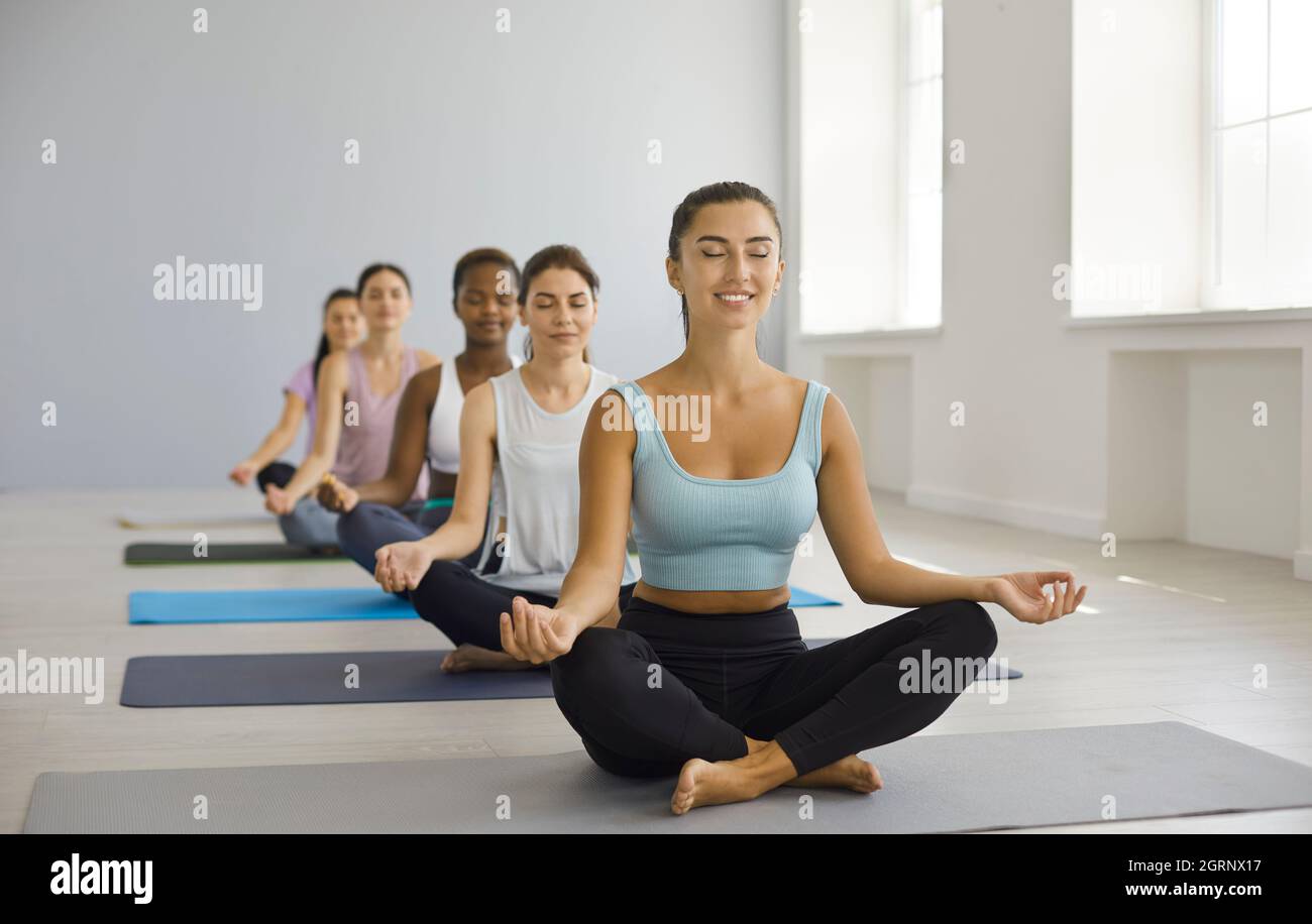 Eine Gruppe von glücklichen, entspannten Frauen, die im Fitnessstudio Yoga-Kurse machten, Lotusposen machten und meditierten Stockfoto