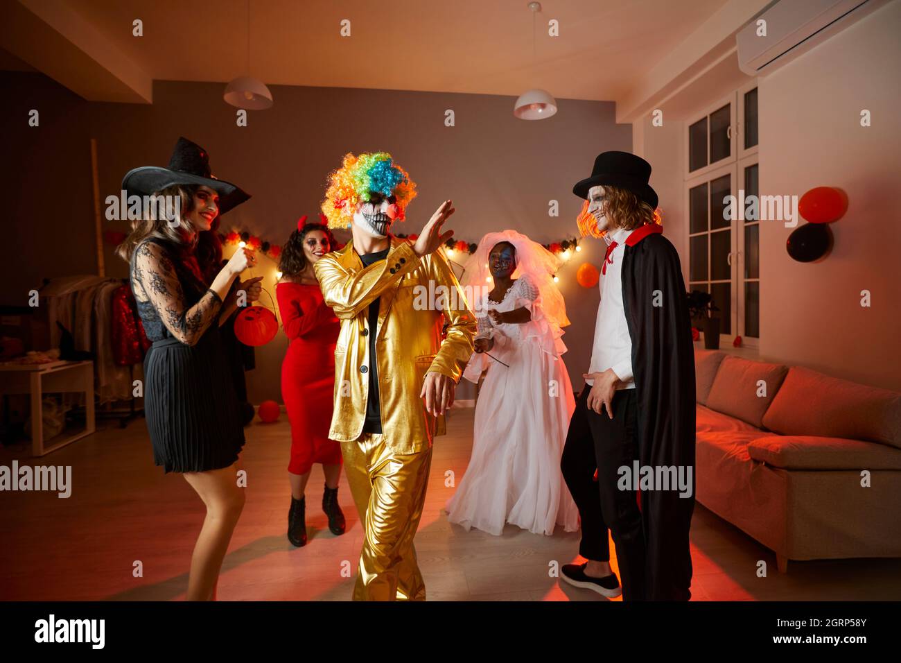 Fröhliche junge Freunde, die in Kostümen verkleidet sind und auf einer lustigen Halloween-Party zu Hause tanzen Stockfoto