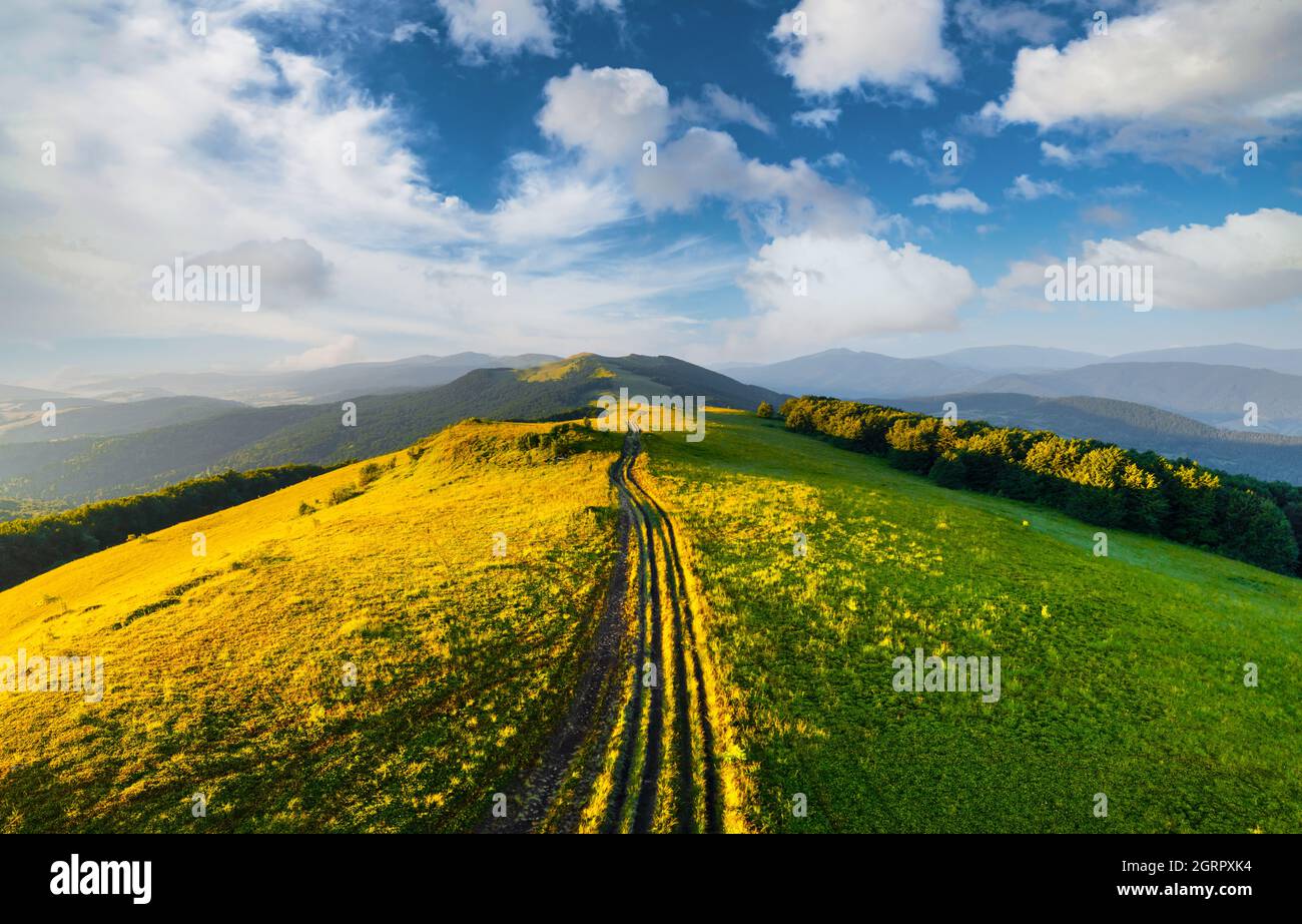 Fantastische Szene auf den Sommerbergen. Grünes Gras, Landstraße und blauer Himmel bei fantastischer Morgensonne. Karpaten, Europa. Landschaftsfotografie Stockfoto
