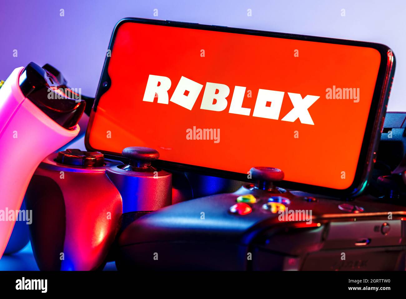 Roblox ist eine Online-Spielplattform und ein System zur Erstellung von Spielen. Ein Smartphone mit dem Roblox-Logo auf dem Bildschirm auf dem Stapel der Gamepads. Stockfoto