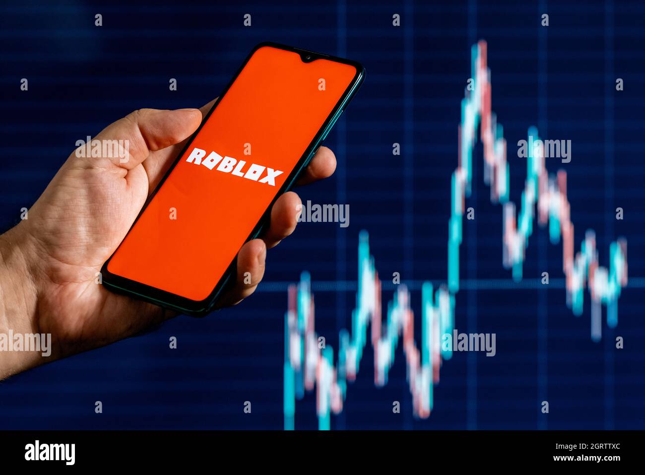 Roblox ist eine Online-Spielplattform und ein System zur Erstellung von Spielen. Ein Smartphone mit dem Roblox-Logo in der Hand. Aktiendiagramm im Hintergrund. Stockfoto