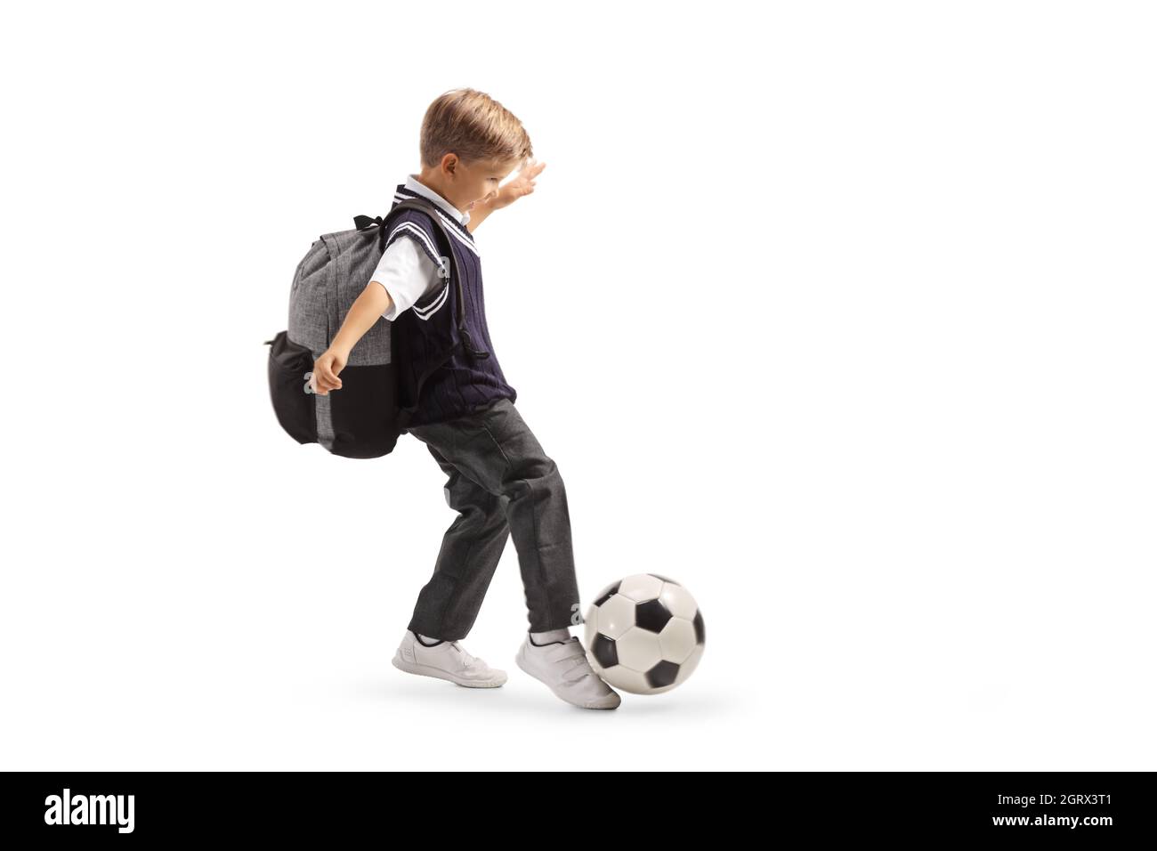 Ganzkörperaufnahme eines Schuljungen in Uniform, der auf weißem Hintergrund isoliert einen Fußballball tritt Stockfoto