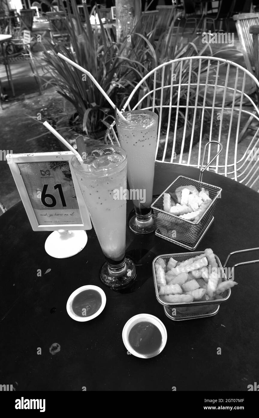 Graustufen-Aufnahme von pommes in Körben auf dem Tisch mit Eisgetränken in einem Café Stockfoto