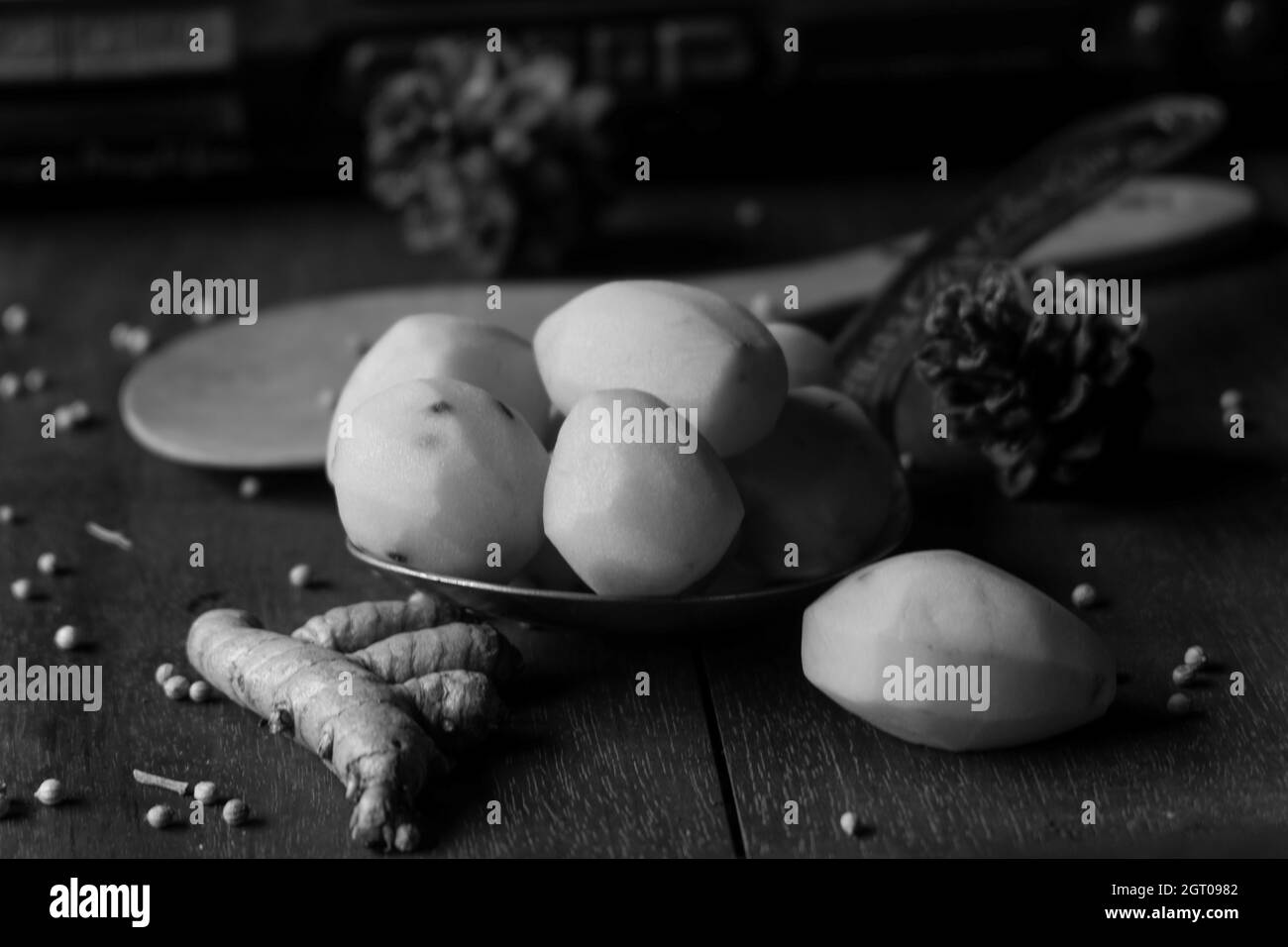 Graustufen-Aufnahme von frischen rohen Kartoffeln und Kurkuma auf dem Tisch mit verschwommenem Hintergrund Stockfoto