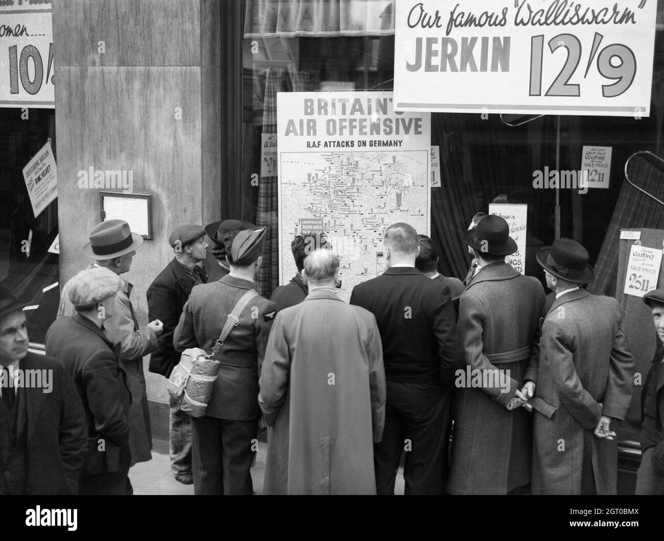 Ein britischer Flieger gehört zu einer Gruppe von Zivilisten, die um das Fenster eines Ladens in Holborn, London, gedrängt sind, um sich eine dort abgestellte Karte mit dem Titel 'Britain's Air Offensive' anzusehen, auf der über 700 Überfälle der Royal Air Force auf Deutschland zu sehen sind. Stockfoto
