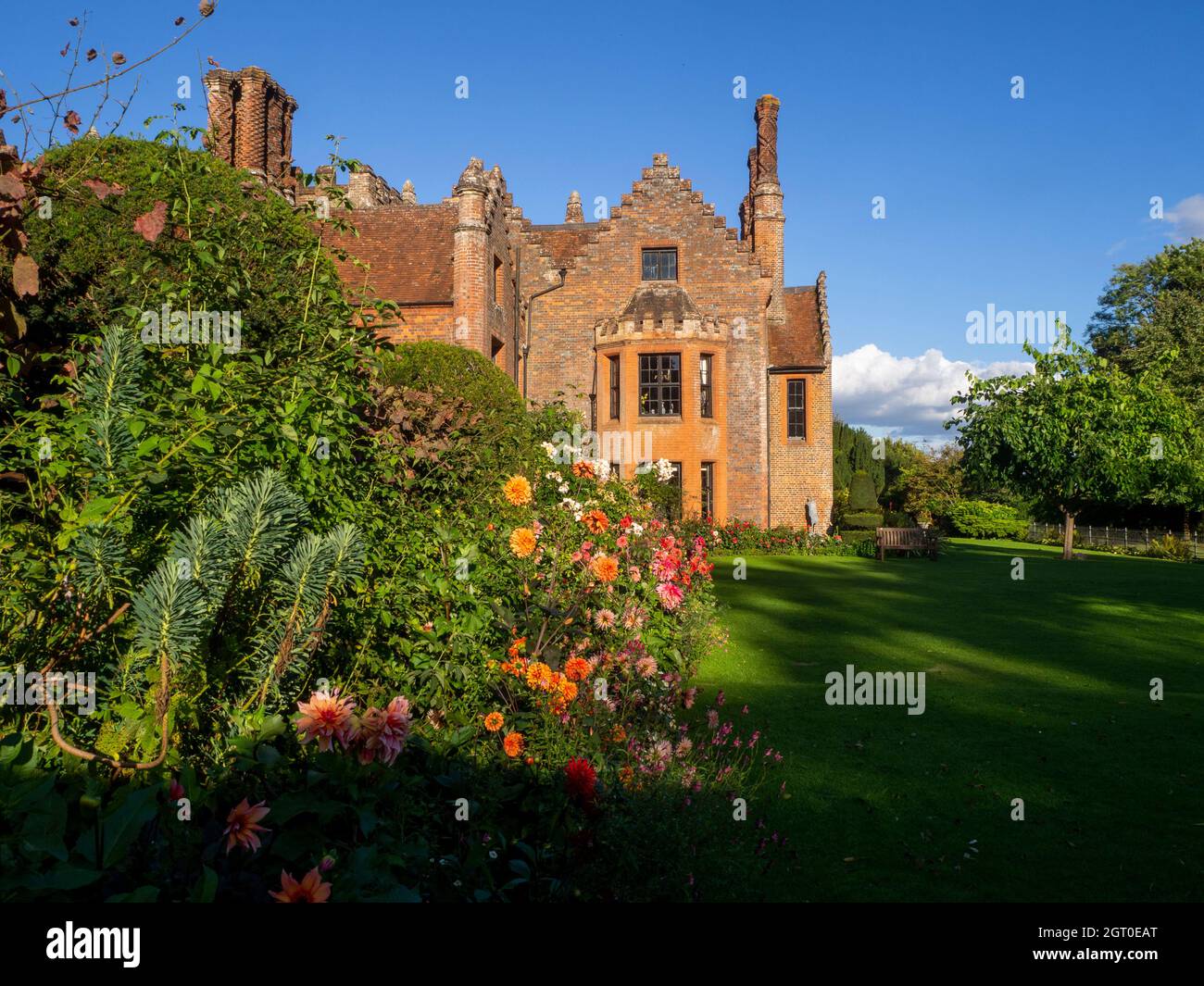 Herrenhaus Chenies im Herbst.Pflanzengrenze mit großen orangefarbenen und rosa Dahlien Blüten führen den Blick auf die Erkerfenster des Tudor Herrenhauses im September. Stockfoto