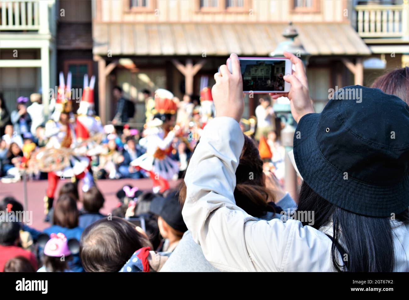 Ein Mädchen in einem schwarzen Eimer Hut steht mit der Menge und macht ein Foto von einer Parade mit ihrem Telefon Stockfoto