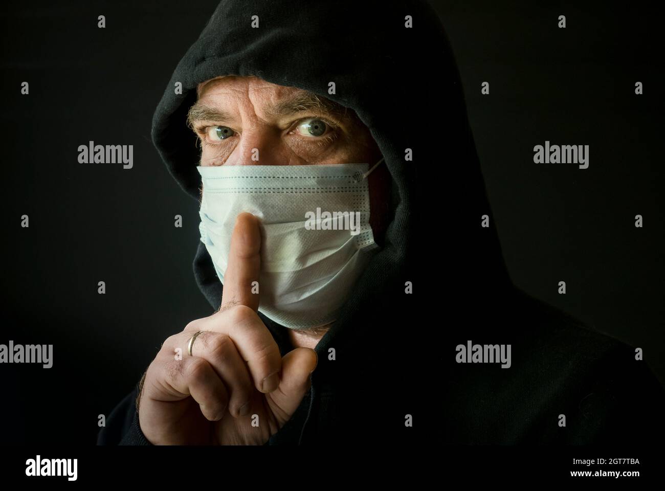 Ein Mann in Einem schwarzen Hoodie und einer medizinischen Maske mit einem Finger am Mund. Coronavirus Conspiracy Konzept Stockfoto