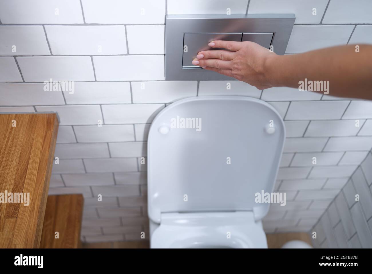 Die weibliche Hand drückt die Spültaste in der Nahaufnahme der Toilette Stockfoto