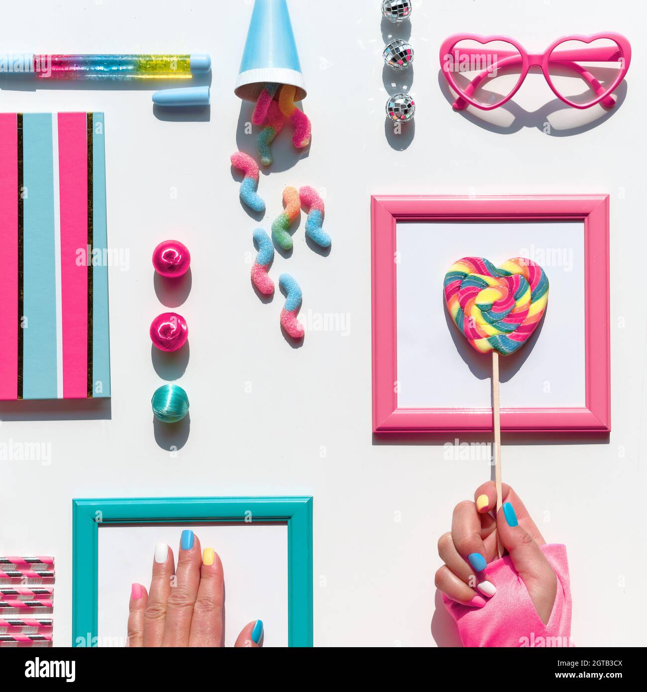 Sammlung von Party-Objekten und Süßigkeiten, Draufsicht, flaches Lay. Schokolade, Süßigkeiten. Notizbuch und Regenbogen-Lolly knallen in der Hand. Festliche geometrische Anordnung in Stockfoto
