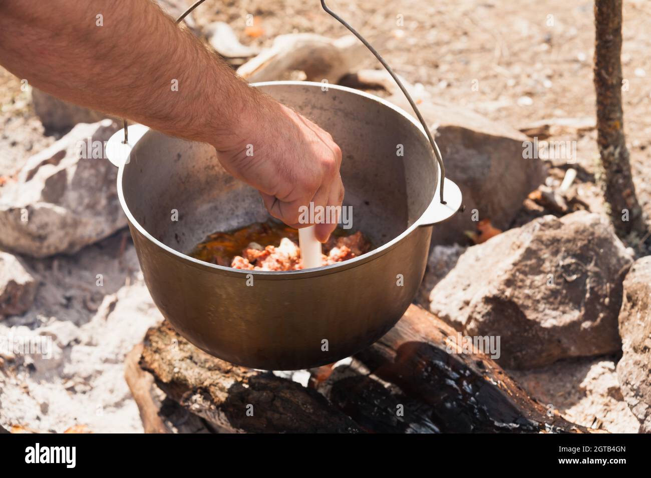 Männliche Hand, die Suppe in einem Kessel mischt. Die Vorbereitung der Mahlzeit auf dem offenen Feuer Stockfoto