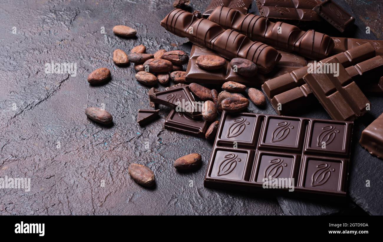 Stücke gebrochener leckerer Milch und dunkler Schokoladentafeln mit Kakaobohnen auf braunem Betongrund Stockfoto