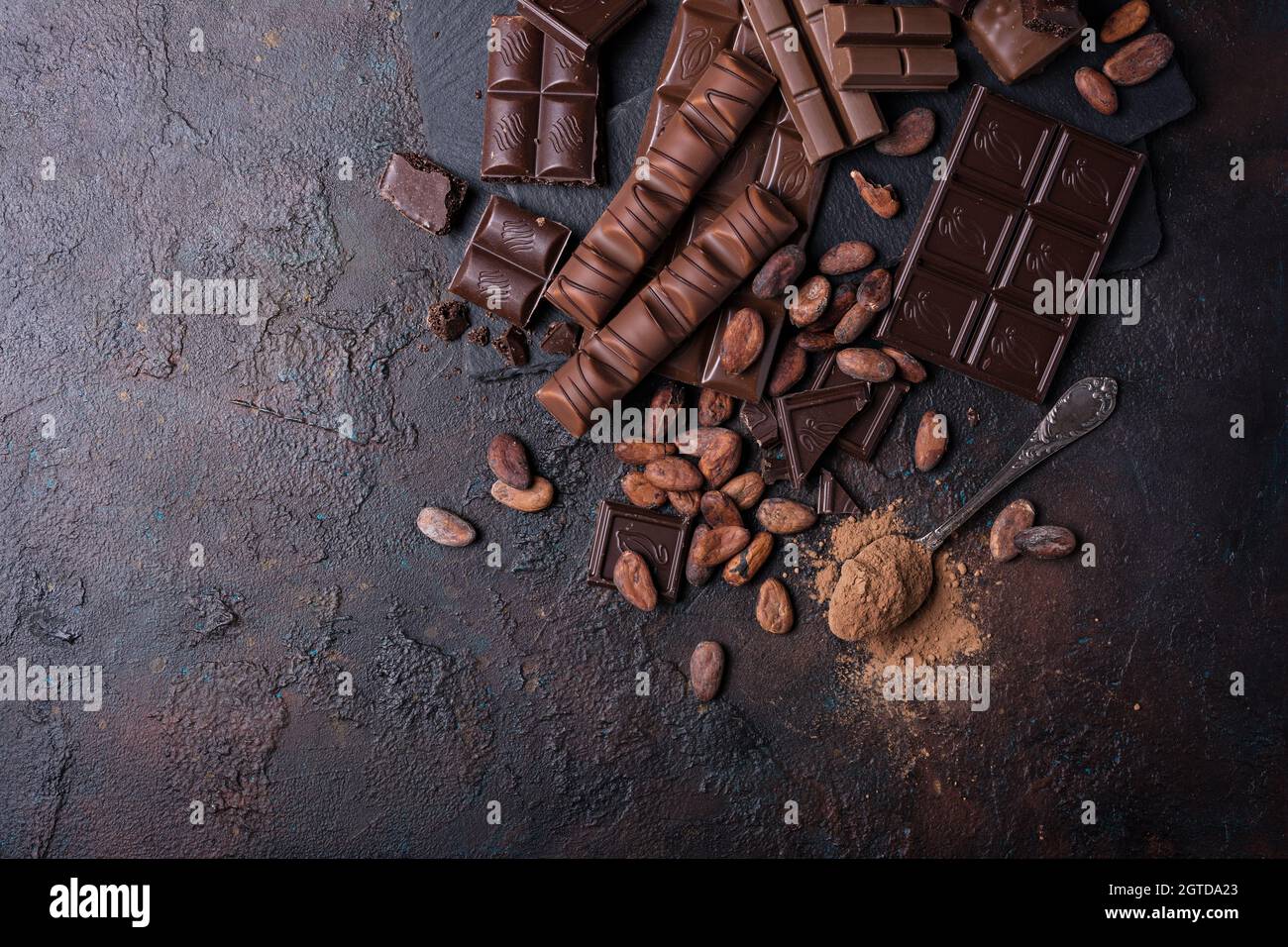 Stücke gebrochener leckerer Milch und dunkler Schokoladentafeln mit Kakaobohnen auf braunem Betongrund Stockfoto