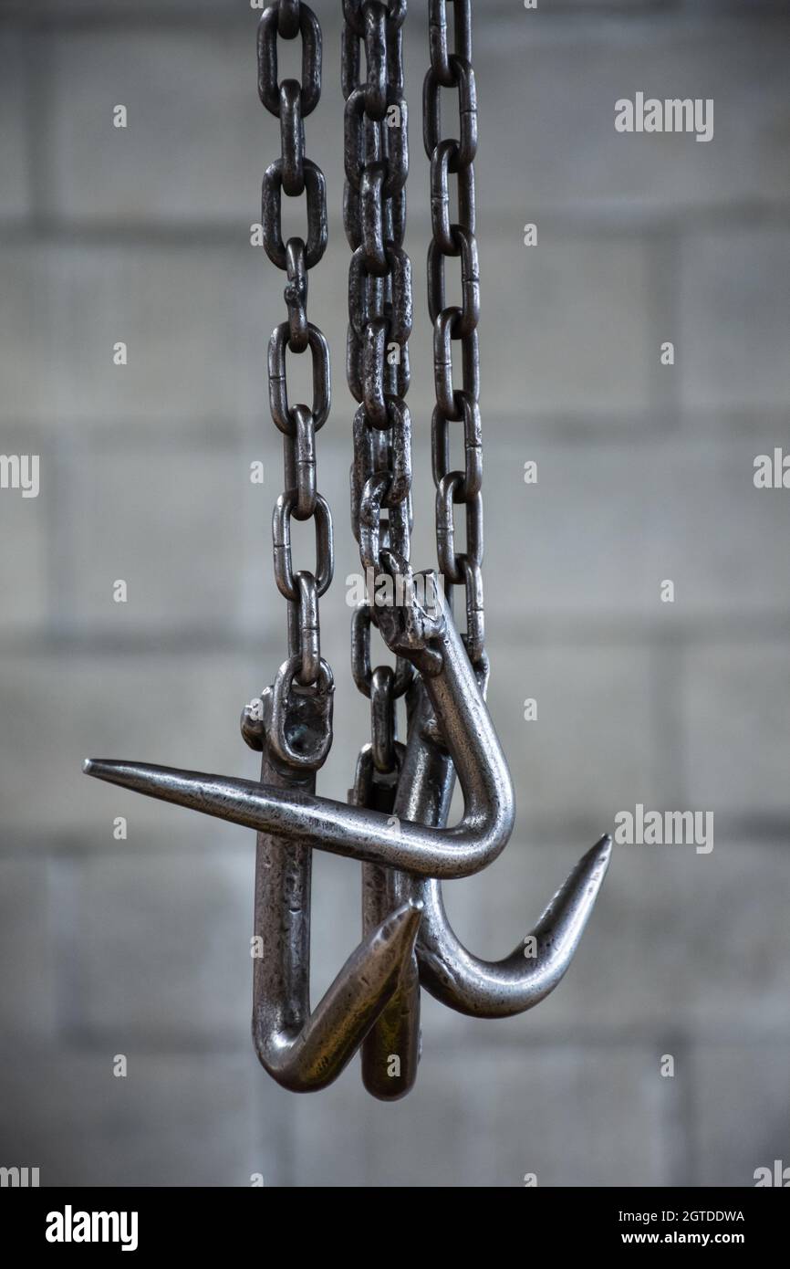 Vertikale Aufnahme von Metallhaken, die an Ketten auf einem grauen Backsteinwand hängen. Stockfoto