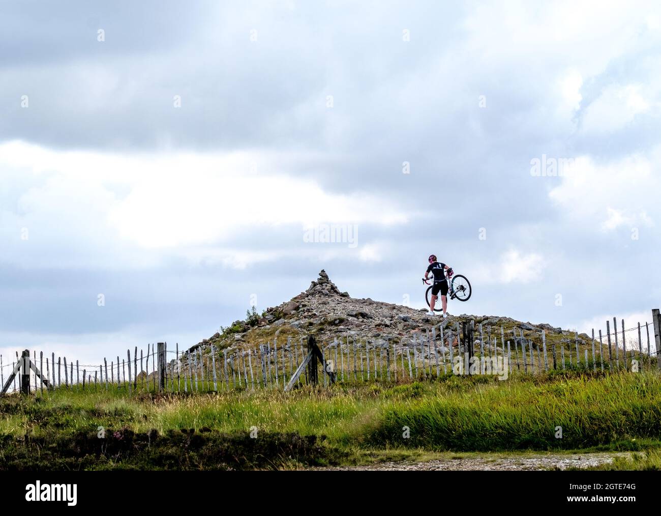 In Cairn O' Mounth, in den Eastern Cairngorms in Aberdeenshire, Schottland, trägt eine Radfahrerin ihr Mountainbike zur Spitze des Cairn. Stockfoto