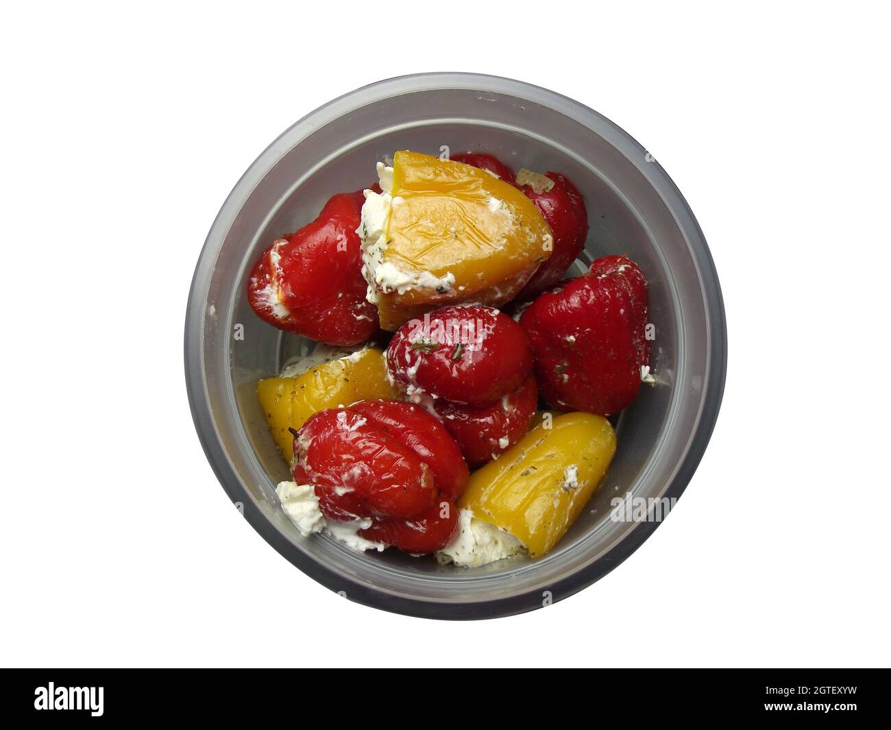 In einem Glas mit offenem Deckel liegt auf einem weißen Teller süße eingelegte Paprika, gefüllt mit weichem Weißkäse und Gewürzen Stockfoto
