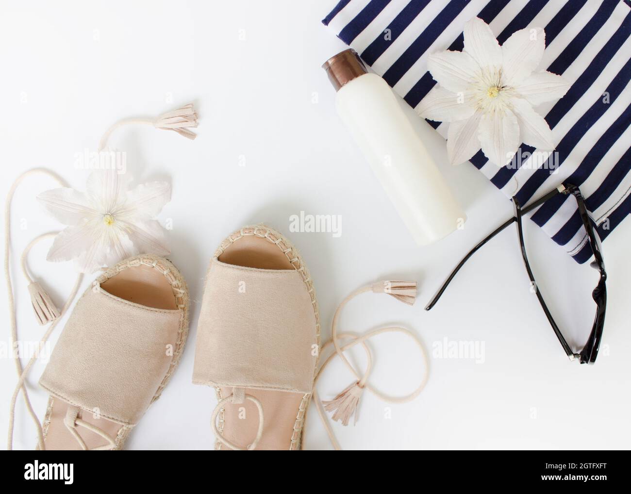 Sommer flach Lay. Sommersandalen, weiße Blumen, Sonnenbrillen und eine weiße Flasche.Draufsicht. Kreativer Hintergrund. Stockfoto