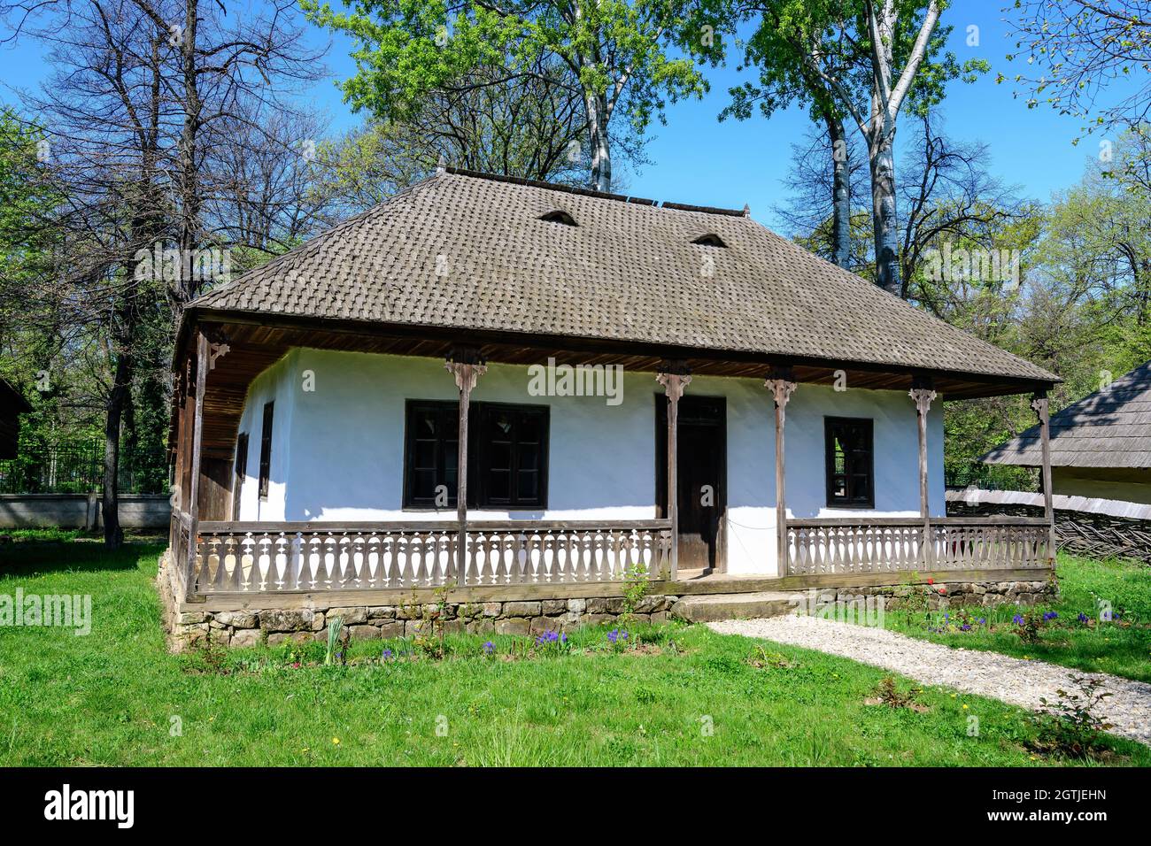 Bukarest, Rumänien - 25. April 2021: Altes traditionelles rumänisches Haus umgeben von vielen alten Bäumen und grünem Gras im Dimitrie Gusti National Village Mu Stockfoto