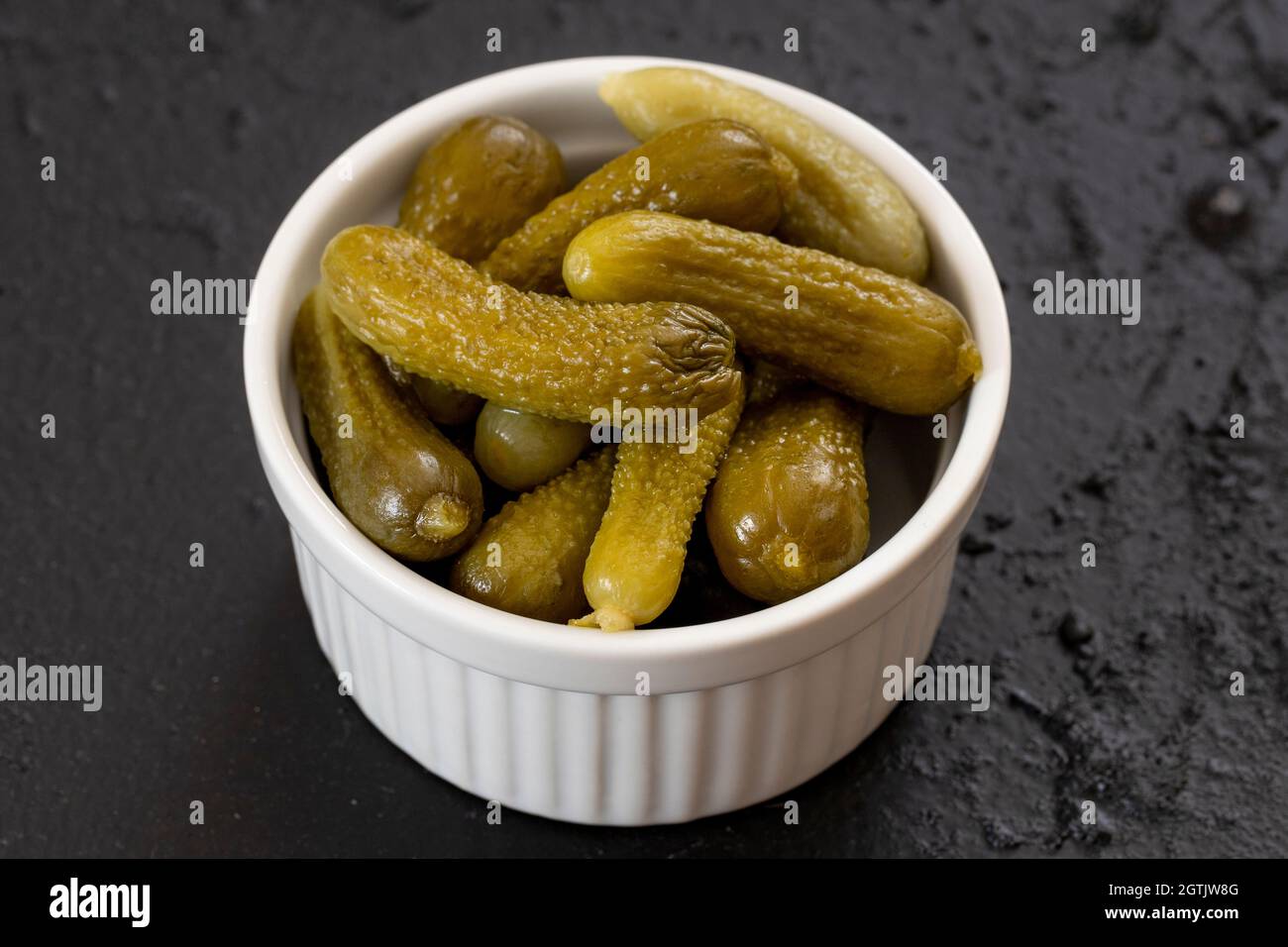 Knusprig eingelegte Cornichons in einer weißen Keramikschale. Marinierte grüne Gurken. Eingelegte Gurke. Leckere Babygurken. Leckeres Gemüse aus der Dose Stockfoto